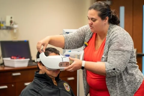 A woman holds a VR headset in place on a man's head