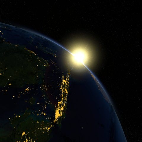 The sun appears above the globe. The land on earth is lit up in the darkness.